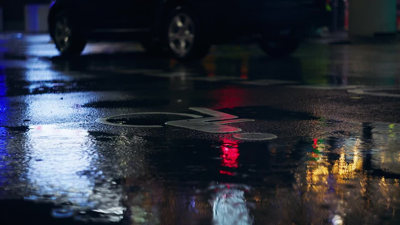 残疾人停车场的夜间标志，闪烁的应急灯反映下雨的路面和经过的卡片视频素材