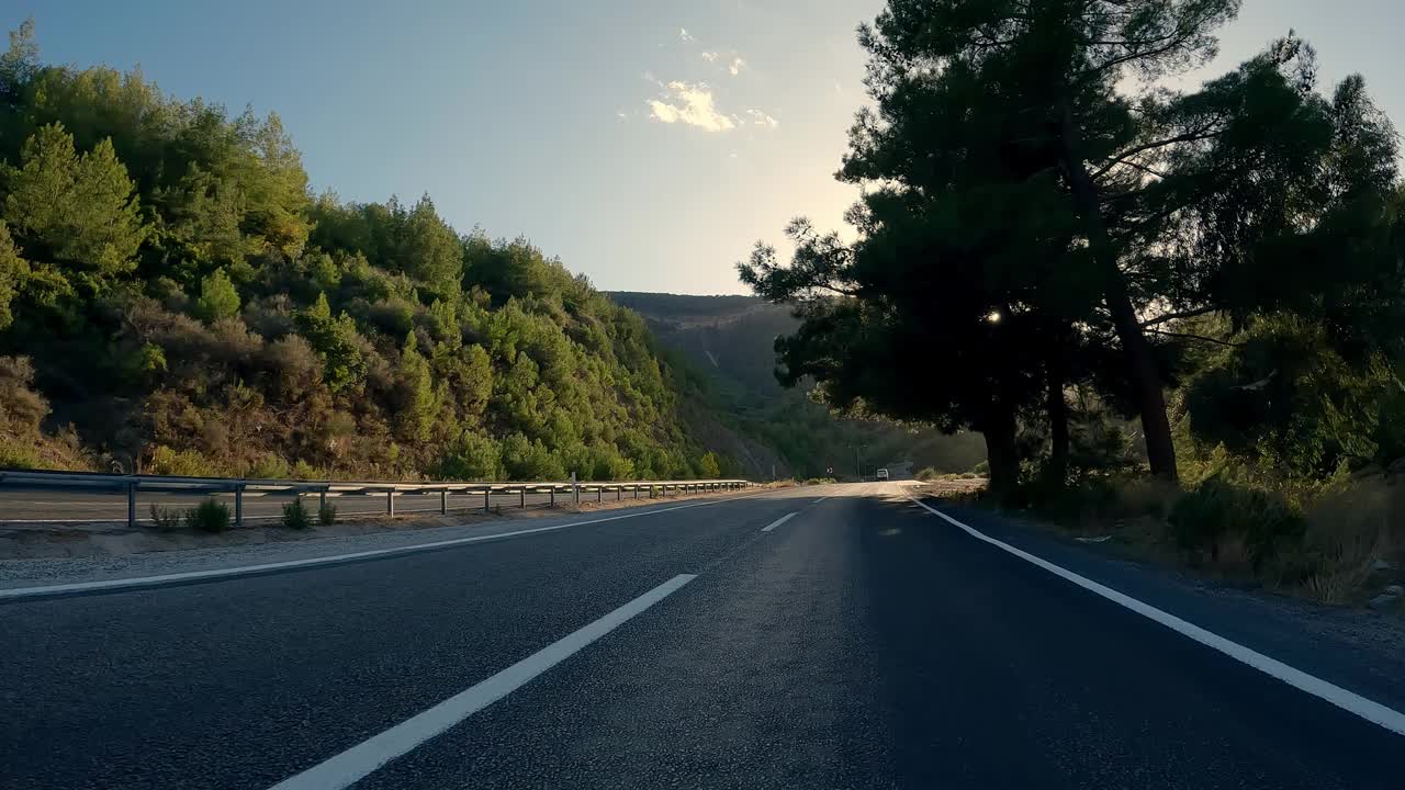 在有黑色沥青和新鲜白色斑纹的山路上行驶。开车旅行，第一人称视角。POV运输前进。阳光照在相机里。视频素材