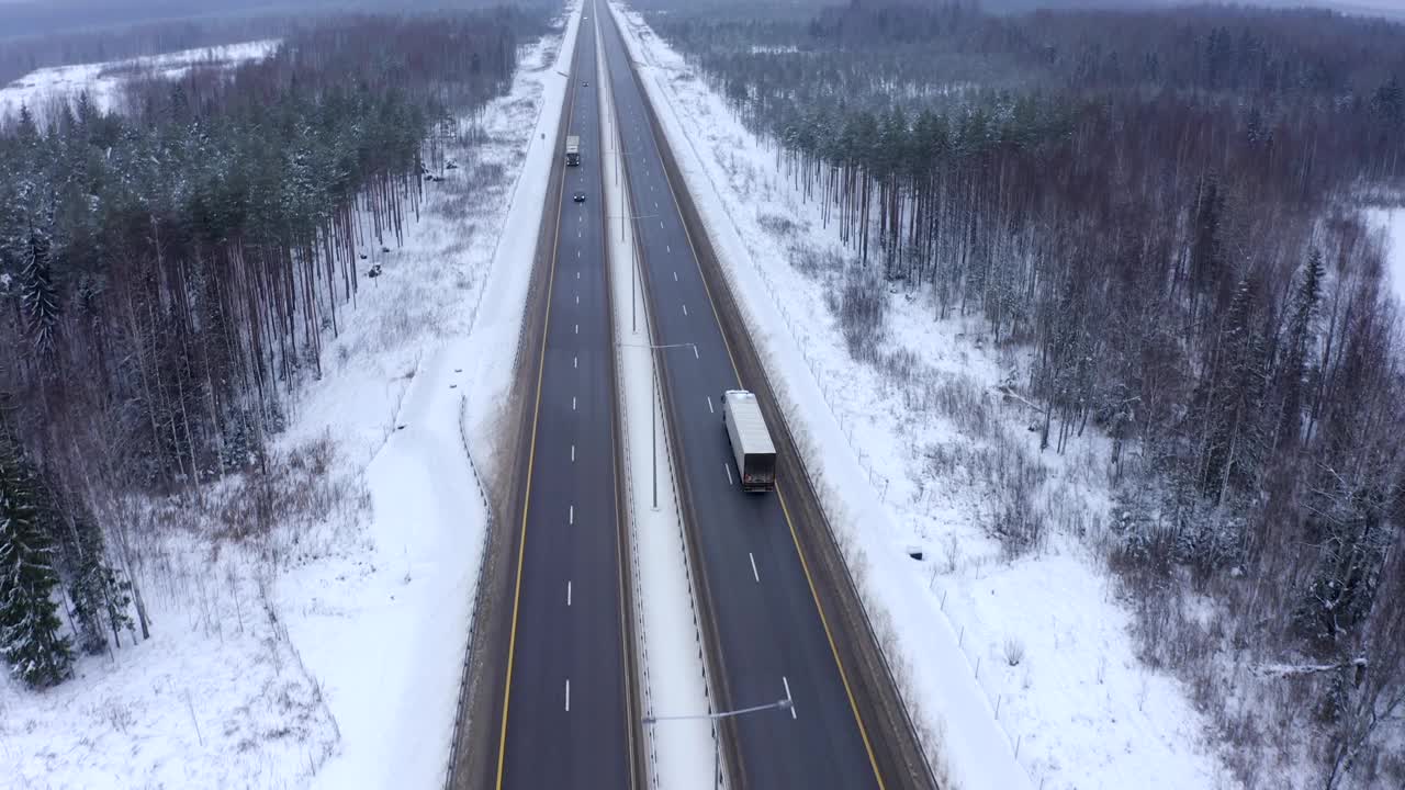 一辆黑色轿车和一辆卡车行驶在白雪覆盖的森林之间的道路上。视频素材