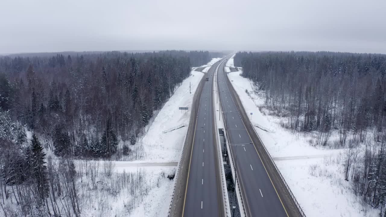 一辆黑色轿车和一辆卡车行驶在白雪覆盖的森林之间的道路上。视频素材