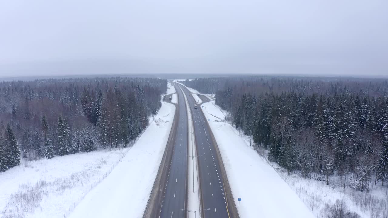 在一个寒冷的冬天，一辆黑色的汽车沿着被雪和雾覆盖的森林中央的道路行驶。视频素材