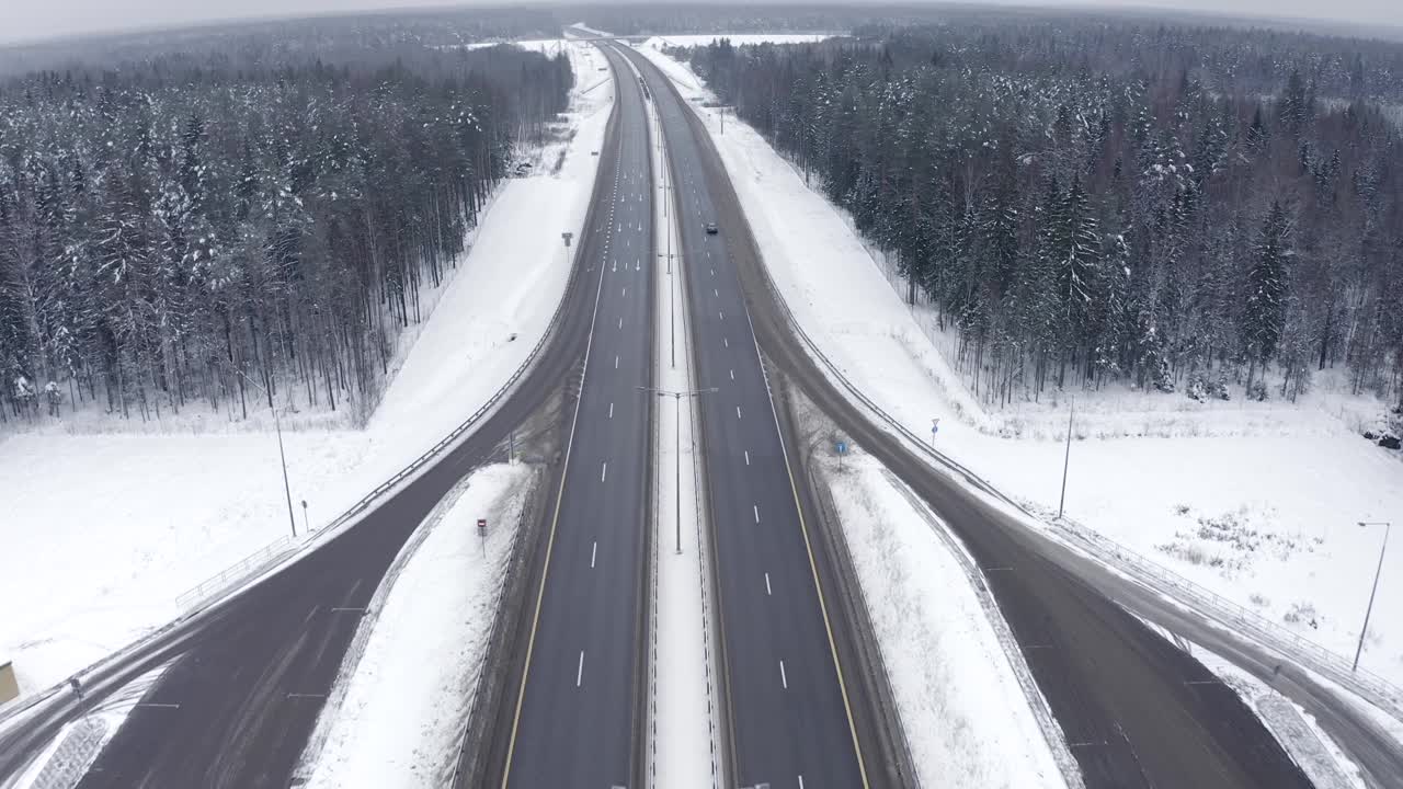 冬天，白雪覆盖的森林中间的高速公路上，一辆路过的黑色汽车视频素材