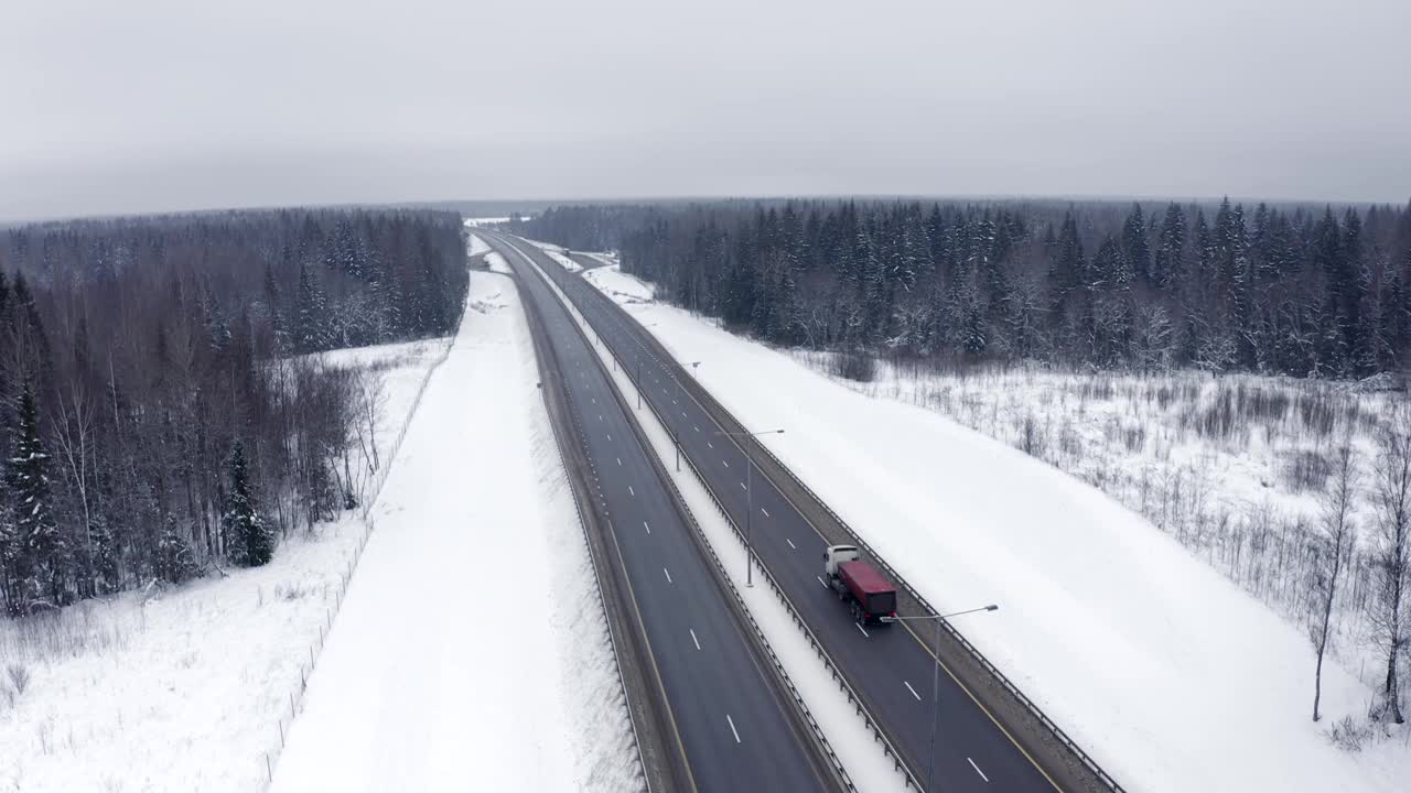 冬天，一辆红色卡车行驶在白雪覆盖的树林间。视频素材