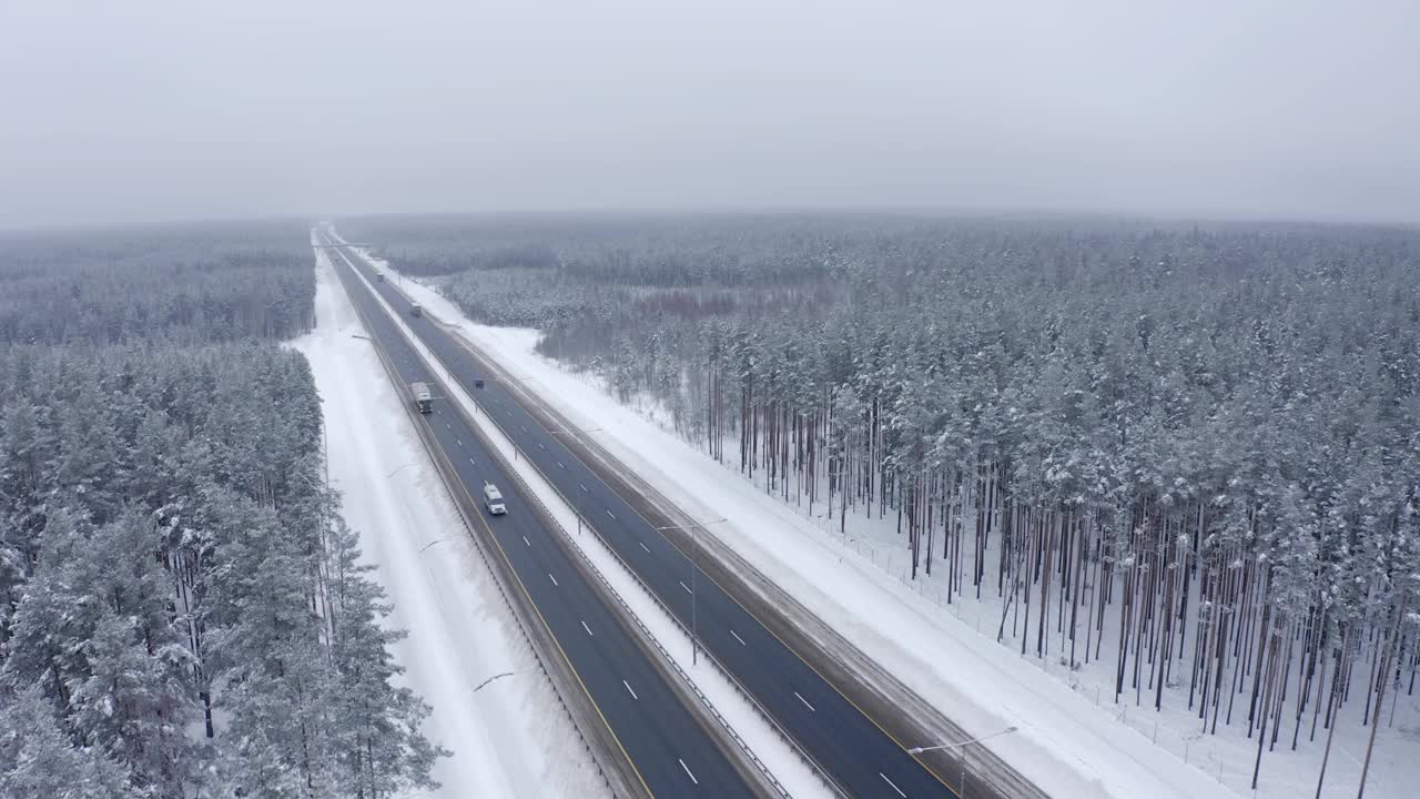 一辆白色货车和一辆卡车行驶在白雪覆盖的森林之间的道路上。视频素材