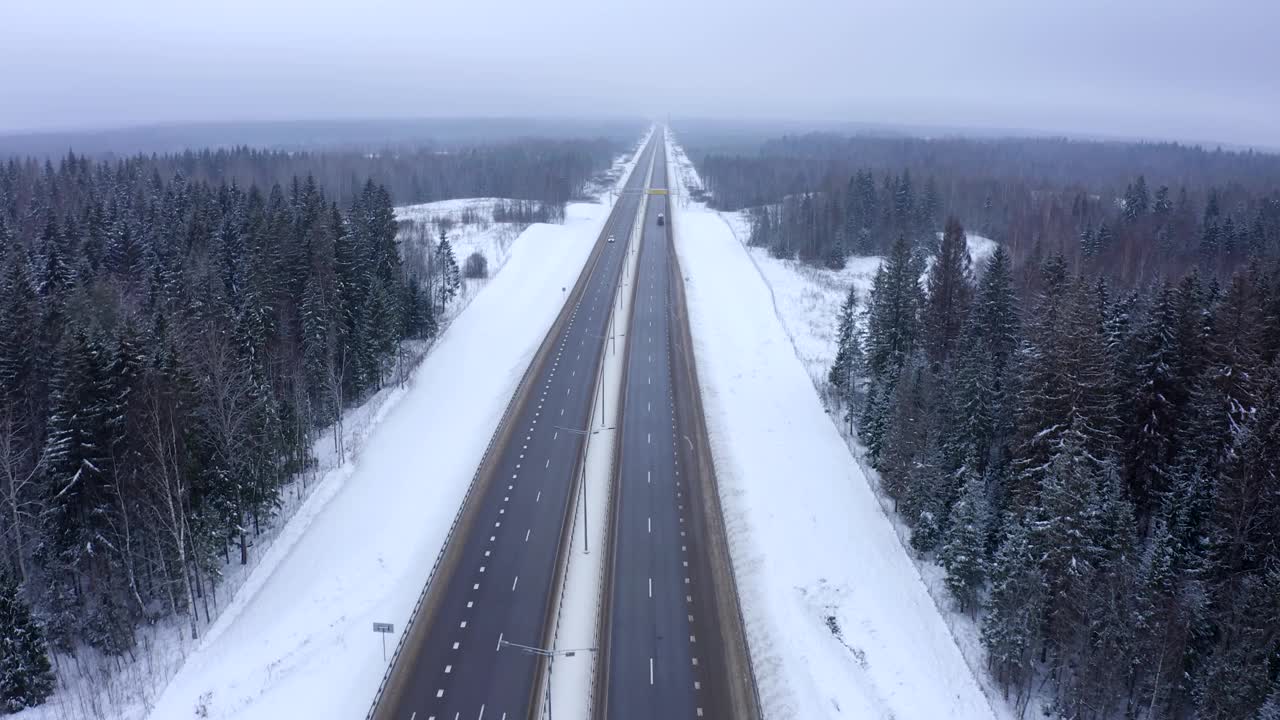 寒冷的冬天，一辆白色货车行驶在白雪覆盖的森林中间的高速公路上。视频素材