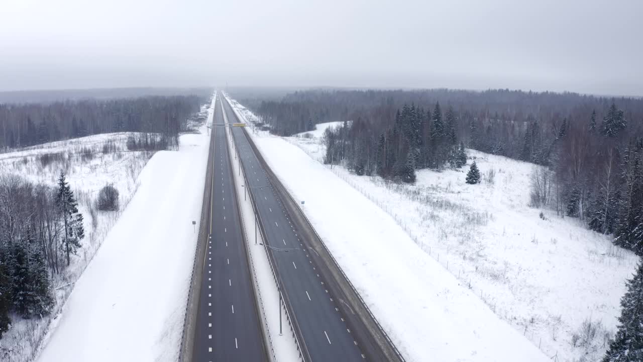 鸟瞰一辆黑色轿车和卡车行驶在白雪覆盖的森林之间的道路上。视频素材