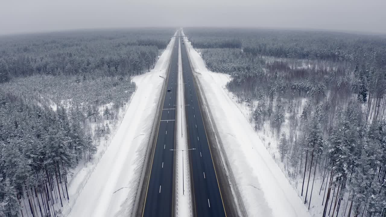 无人机在冬天的道路上飞行，路上有白雪皑皑的森林和一辆路过的黑色汽车视频素材