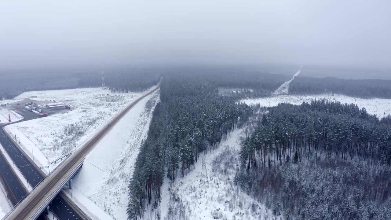 在一个寒冷的冬天，一辆黑色汽车从森林中行驶在一条积雪的道路上。视频素材