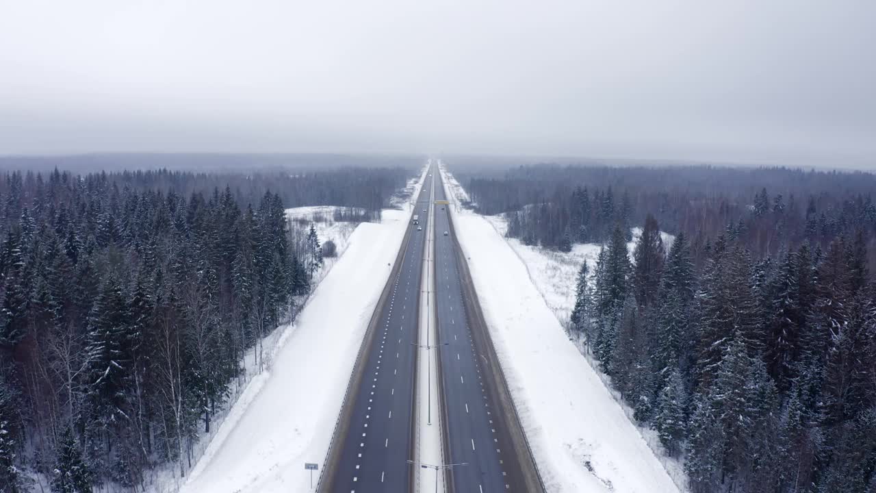 高速公路上行驶着白色和蓝色的汽车，在冬天被雪和雾覆盖的森林中间。视频素材