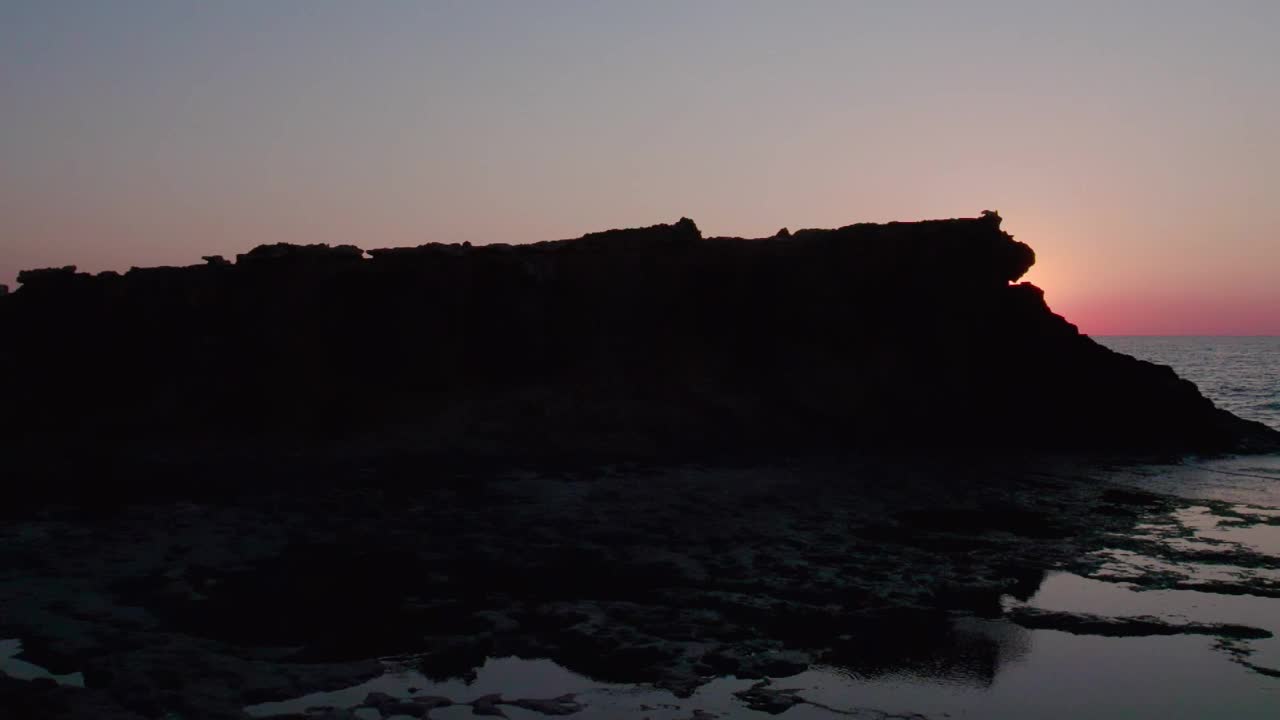 在初升的太阳照耀下，海边岩石的景色。落日的颜色映照在大海的波浪上。视频素材