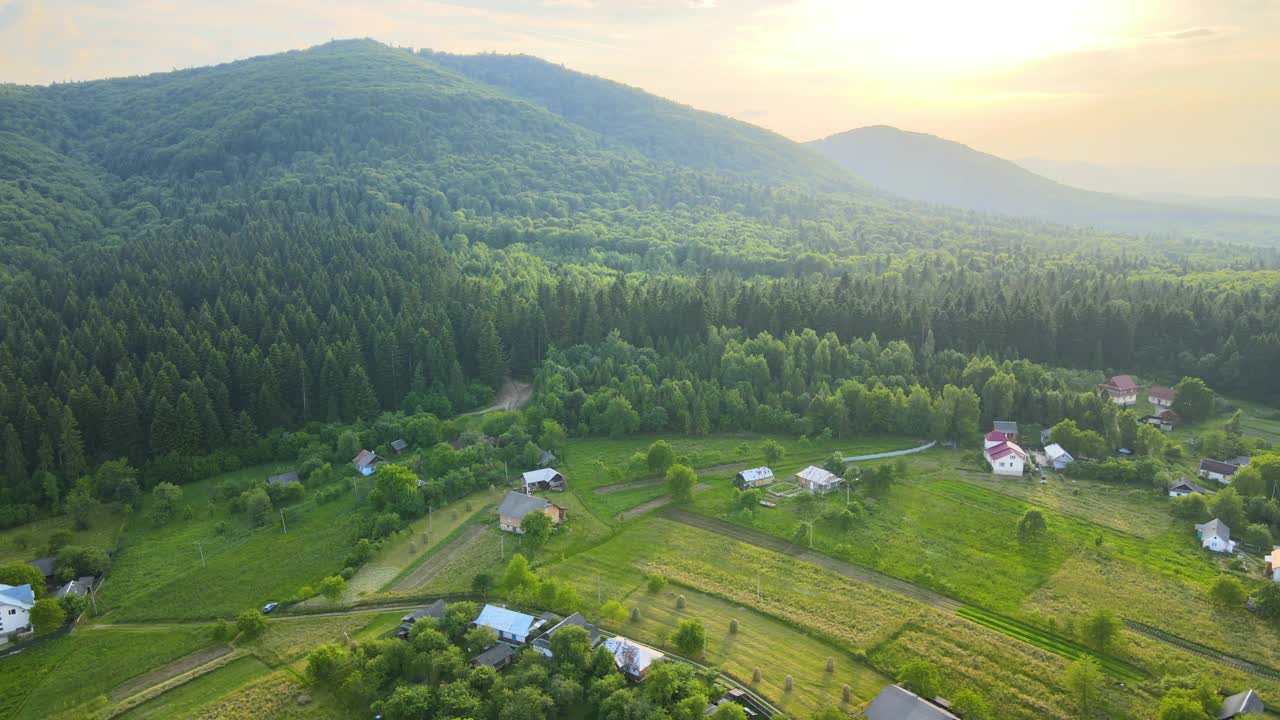 秋天日出时，鸟瞰图上的小村庄房屋在雾蒙蒙的黑暗山峰之间，山顶上覆盖着森林松树。美丽的野生林地，黎明时分的阳光熠熠生辉视频素材