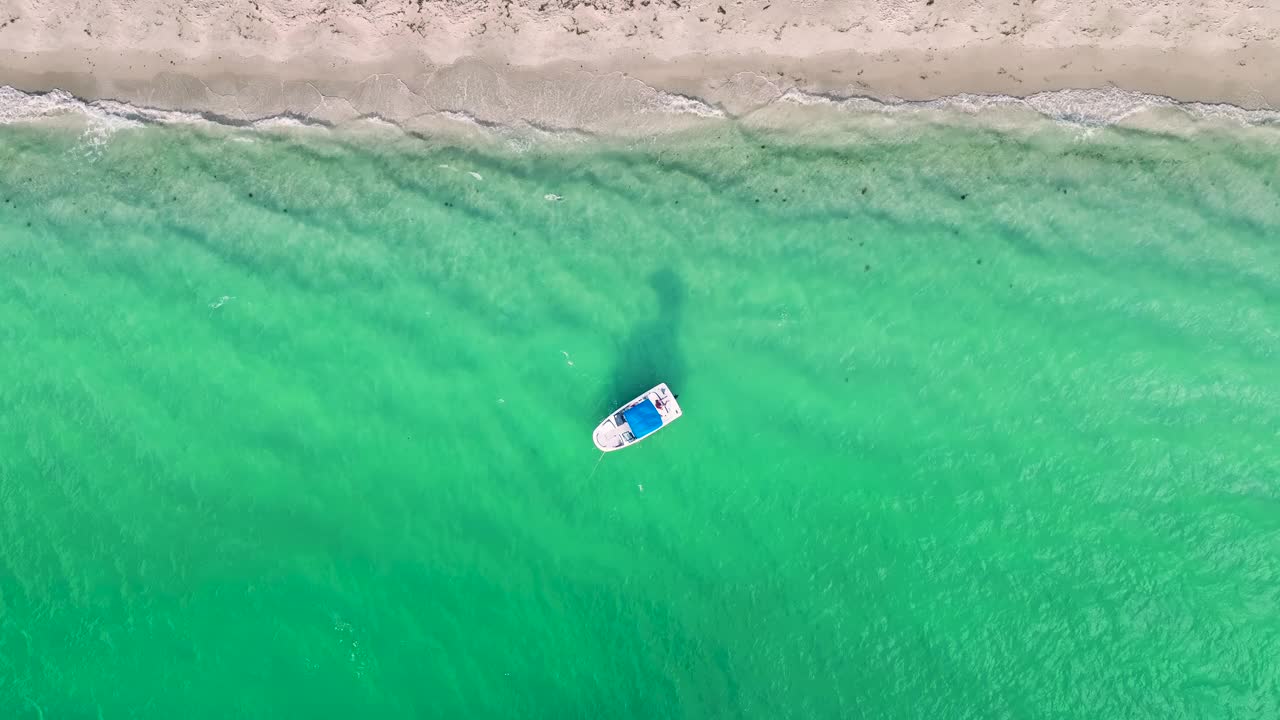 鸟瞰图的小白色摩托艇漂浮在海浪与波纹表面附近的沙滩。海面摩托艇娱乐视频素材