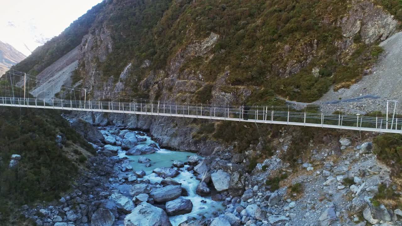 徒步旅行者沿着悬索桥在奔流的河流激流到雪山视频素材