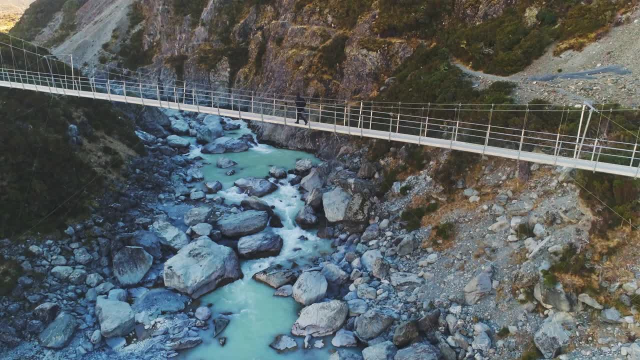 徒步旅行者沿着悬索桥在奔流的河流激流到雪山视频素材