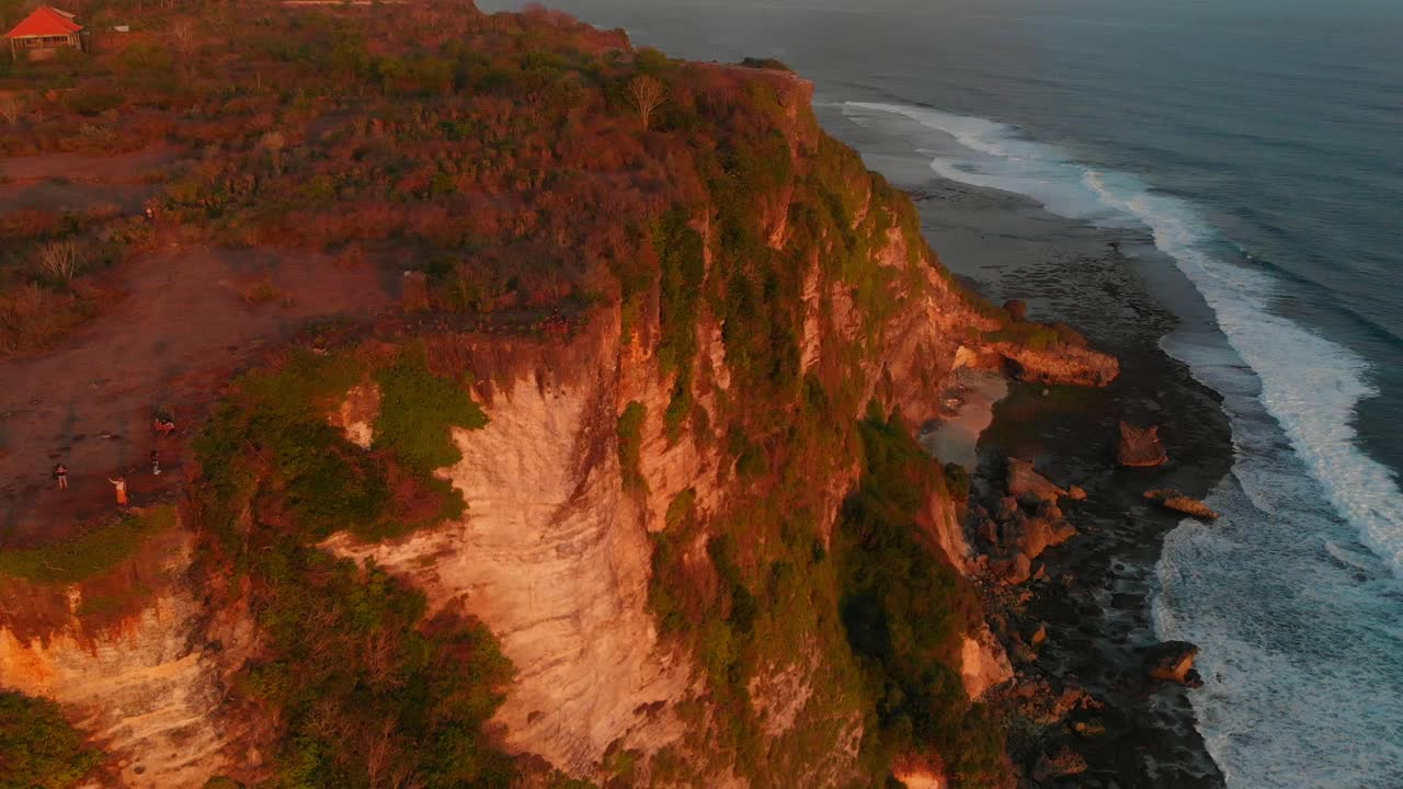 悬崖海岸线的鸟瞰图与海洋在温暖的日落色调在乌鲁瓦图，巴厘岛视频素材