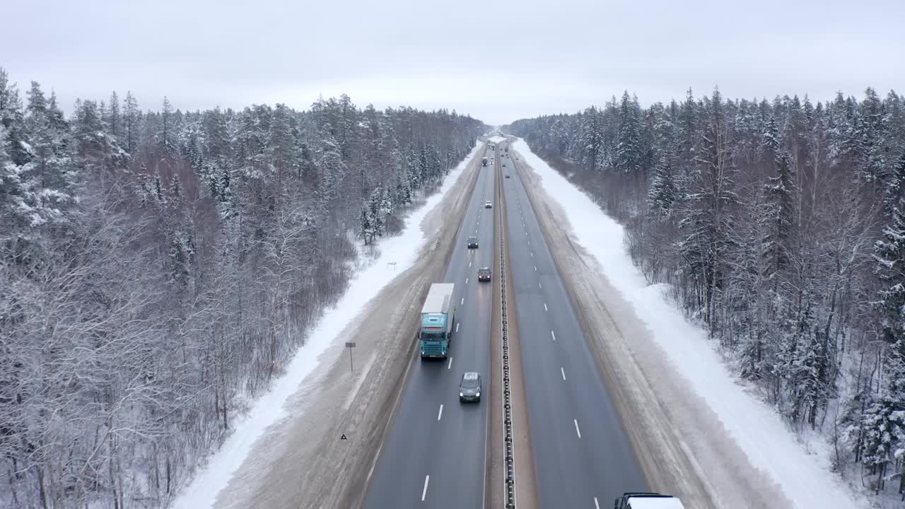 一辆白色汽车行驶在白雪覆盖的森林里的高速公路上。视频素材