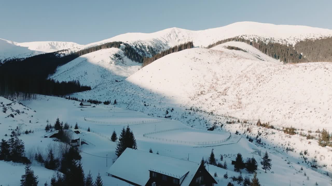 无人机飞越两个冰雪覆盖的冰球场，向美丽的寒冷、阳光明媚的冬季景观山脉飞去。视频素材