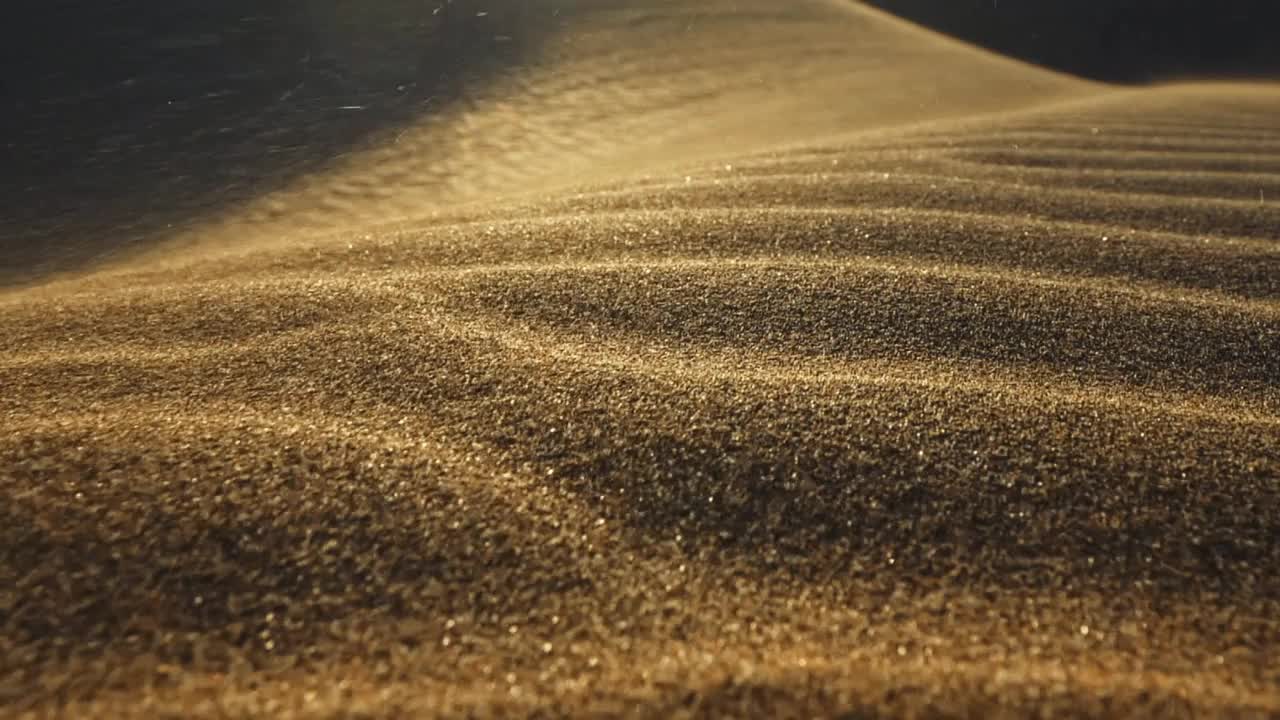 沙漠中的沙尘暴。微距拍摄的沙粒被风吹走。在落日的余晖中，摄像机沿着沙漠中的沙丘表面移动。沙子在风中飘动。慢镜头视频素材