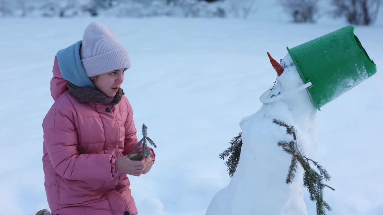 小女孩在寒冷的冬天堆雪人。孩子用冷杉树枝做手视频素材