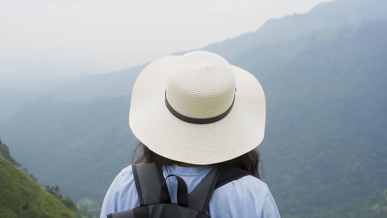 戴着帽子和背包的女游客在雾中欣赏热带山脉。视频素材