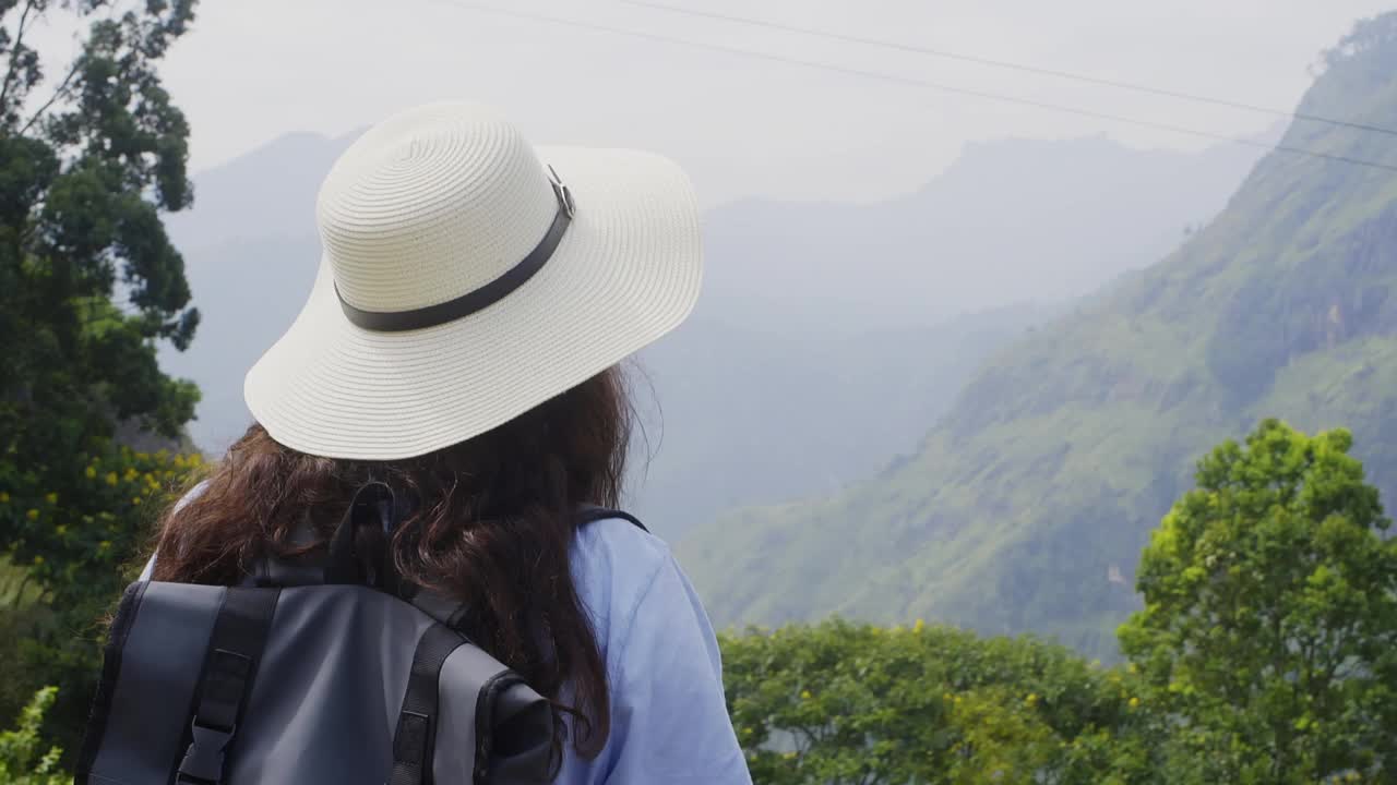 女游客戴着帽子，背着背包，在峡谷中欣赏群山。视频素材