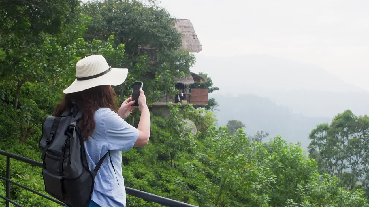 女游客正在用智能手机拍摄山谷和村庄的照片。视频素材