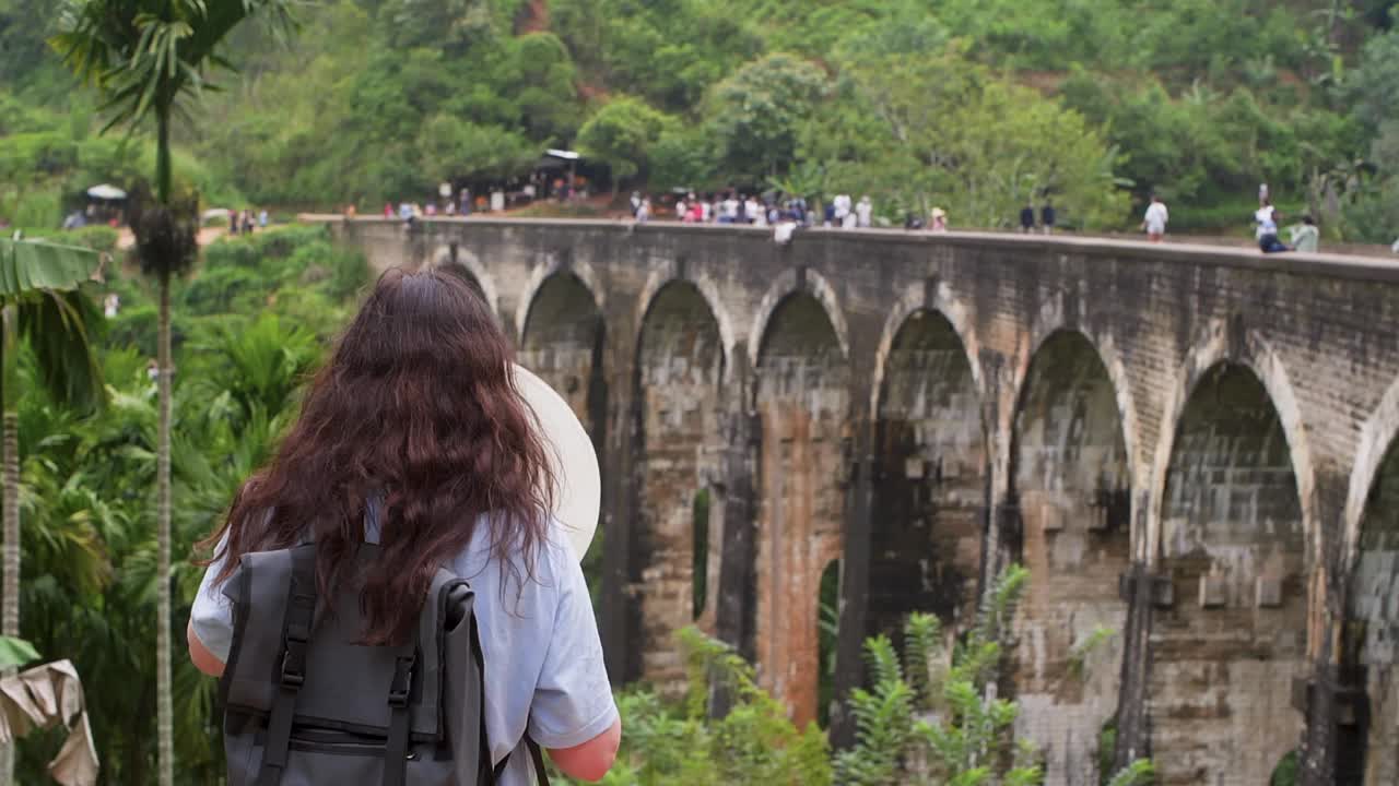 一位女游客正戴上帽子欣赏热带地区的拱桥。视频素材