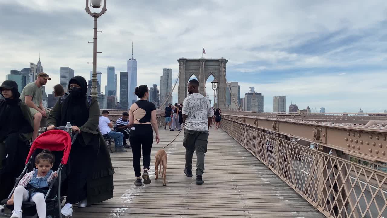 在一个炎热的夏天，成群的行人和游客走过路边的摊贩，穿过标志性的布鲁克林大桥。概念大众旅游城市纽约曼哈顿国际城市人和游客视频素材