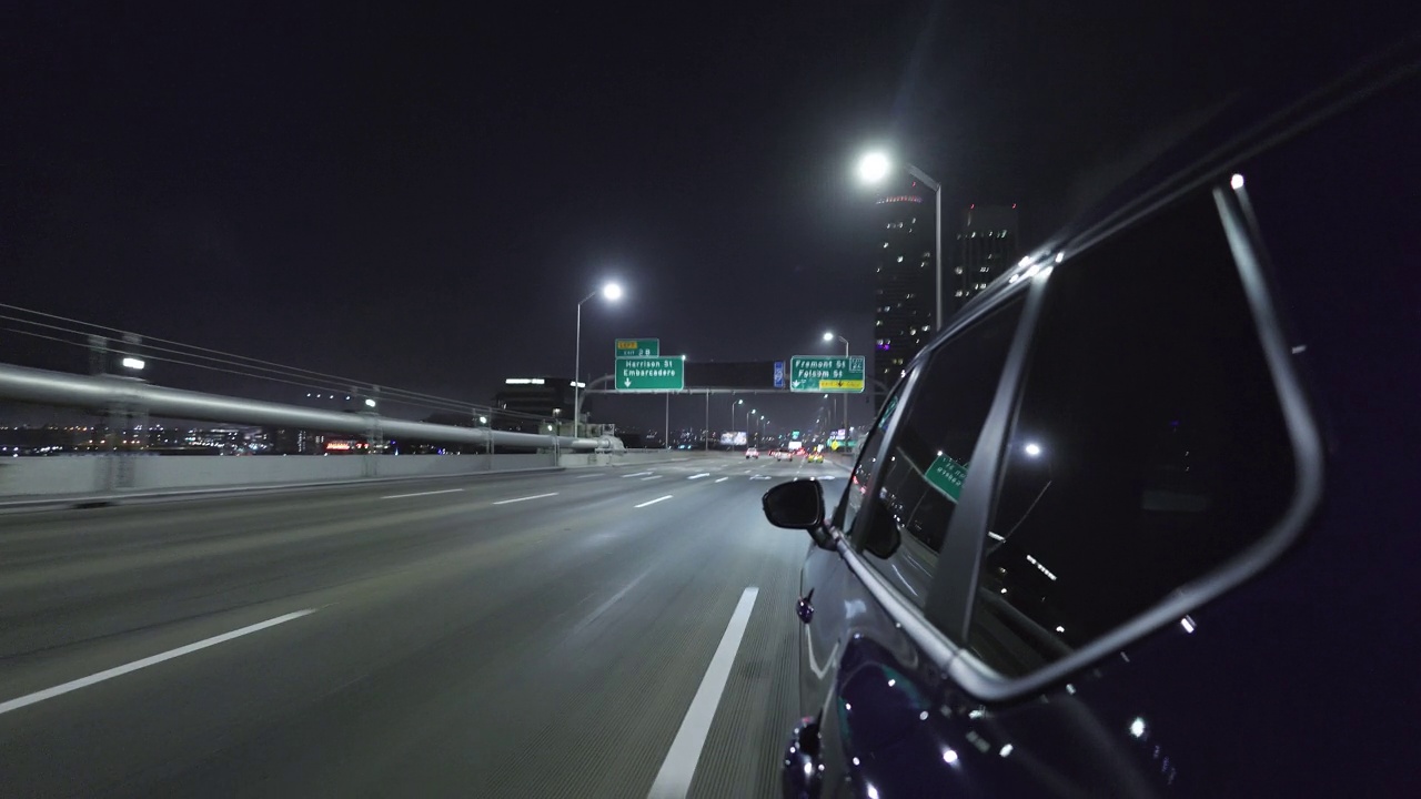 一辆电动汽车行驶在灯火通明的海湾大桥上，驶进夜晚的城市旧金山。视频素材