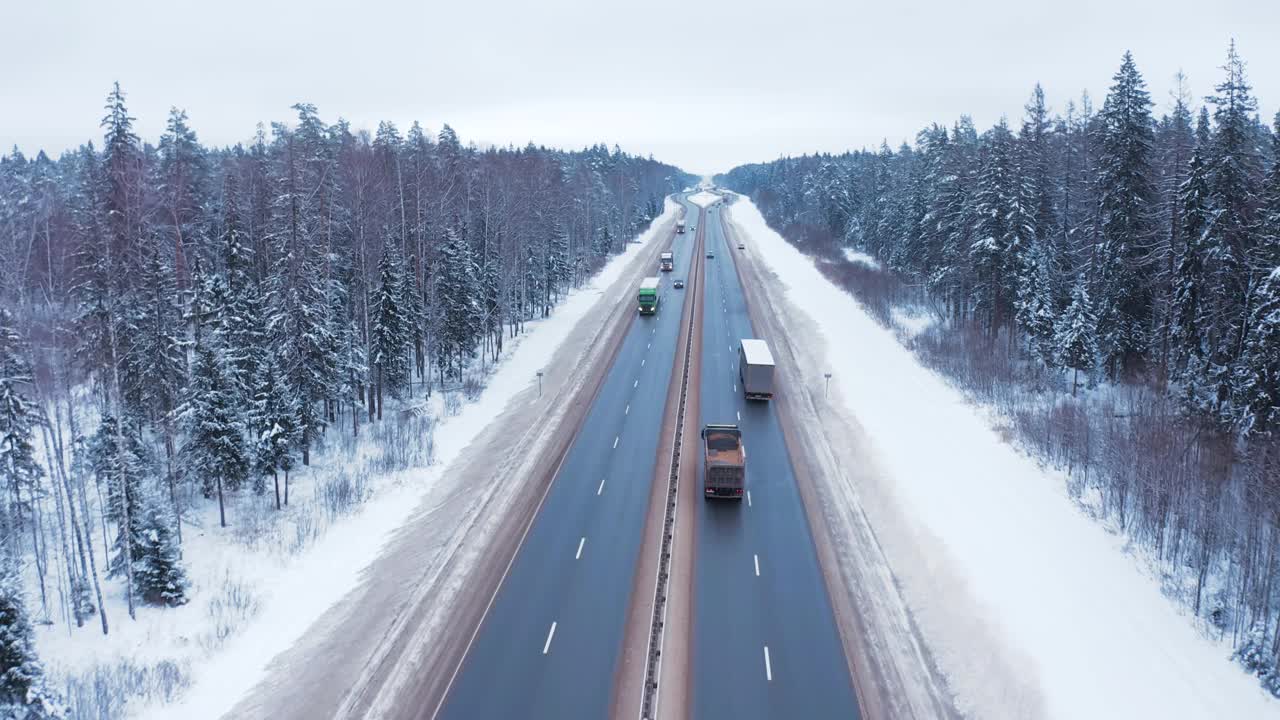 一辆黑色轿车和一辆卡车行驶在白雪覆盖的森林中央的道路上。视频素材