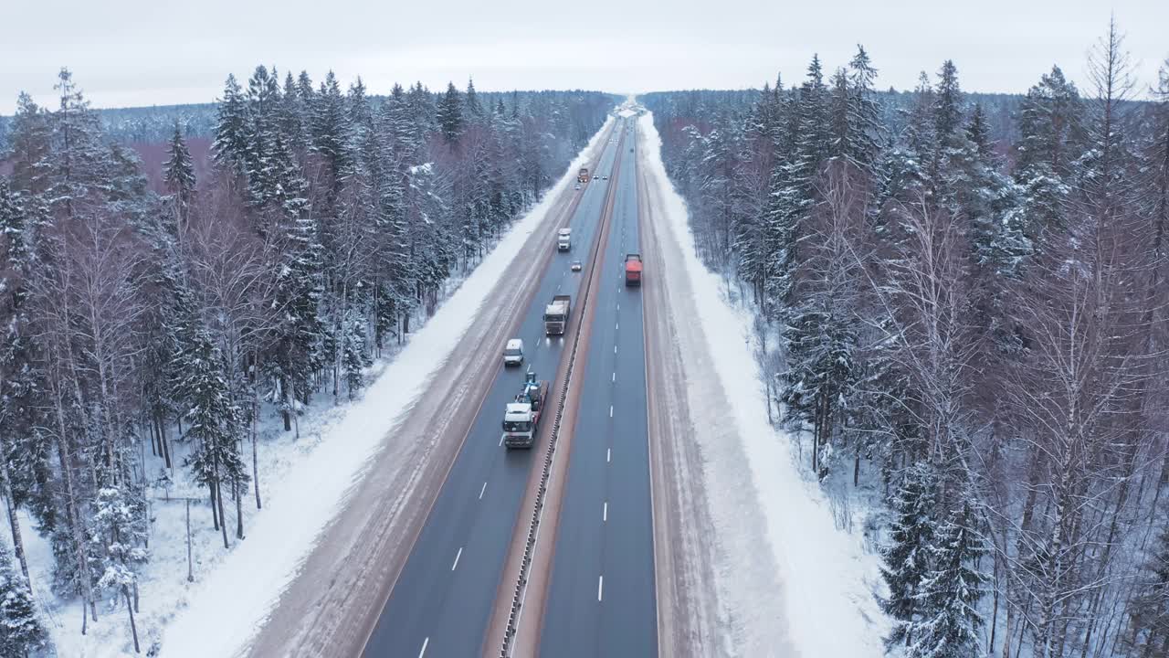 一辆黑白相间的小汽车和一辆卡车行驶在白雪覆盖的森林中央的道路上。视频素材