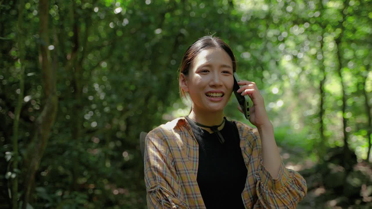 年轻的亚洲女性在热带雨林中使用手机与朋友交谈，无界的通信概念，技术和通信视频素材