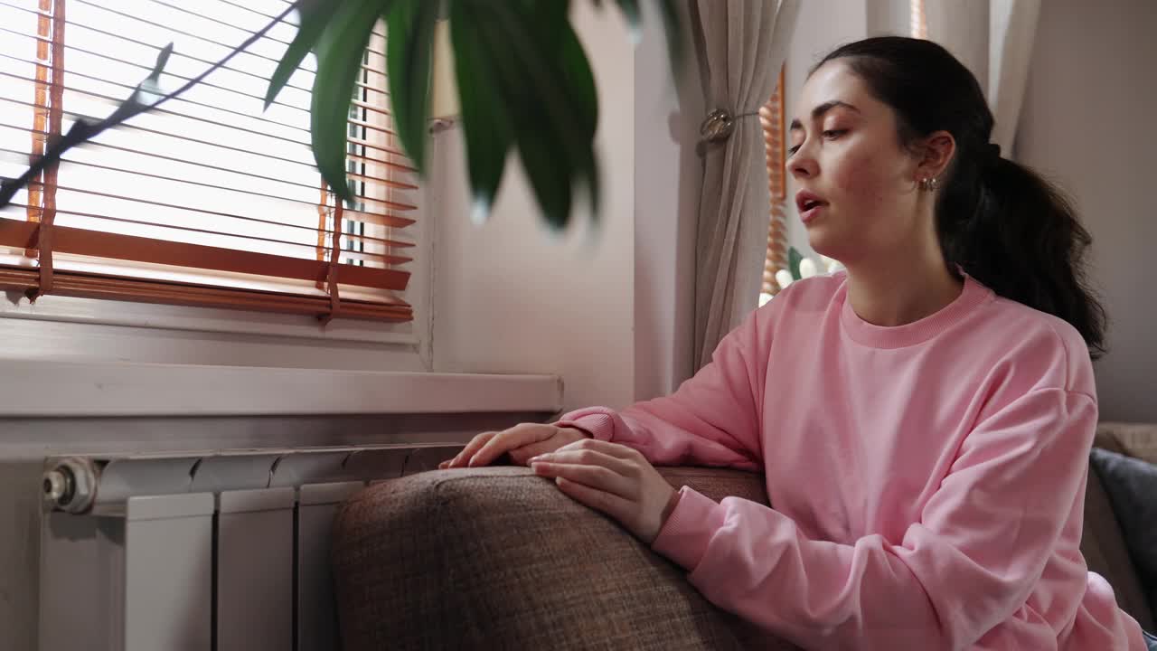 冬季采暖季节。侧面的年轻白人妇女温暖她的手附近的中央加热器散热器。能源危机的概念视频素材