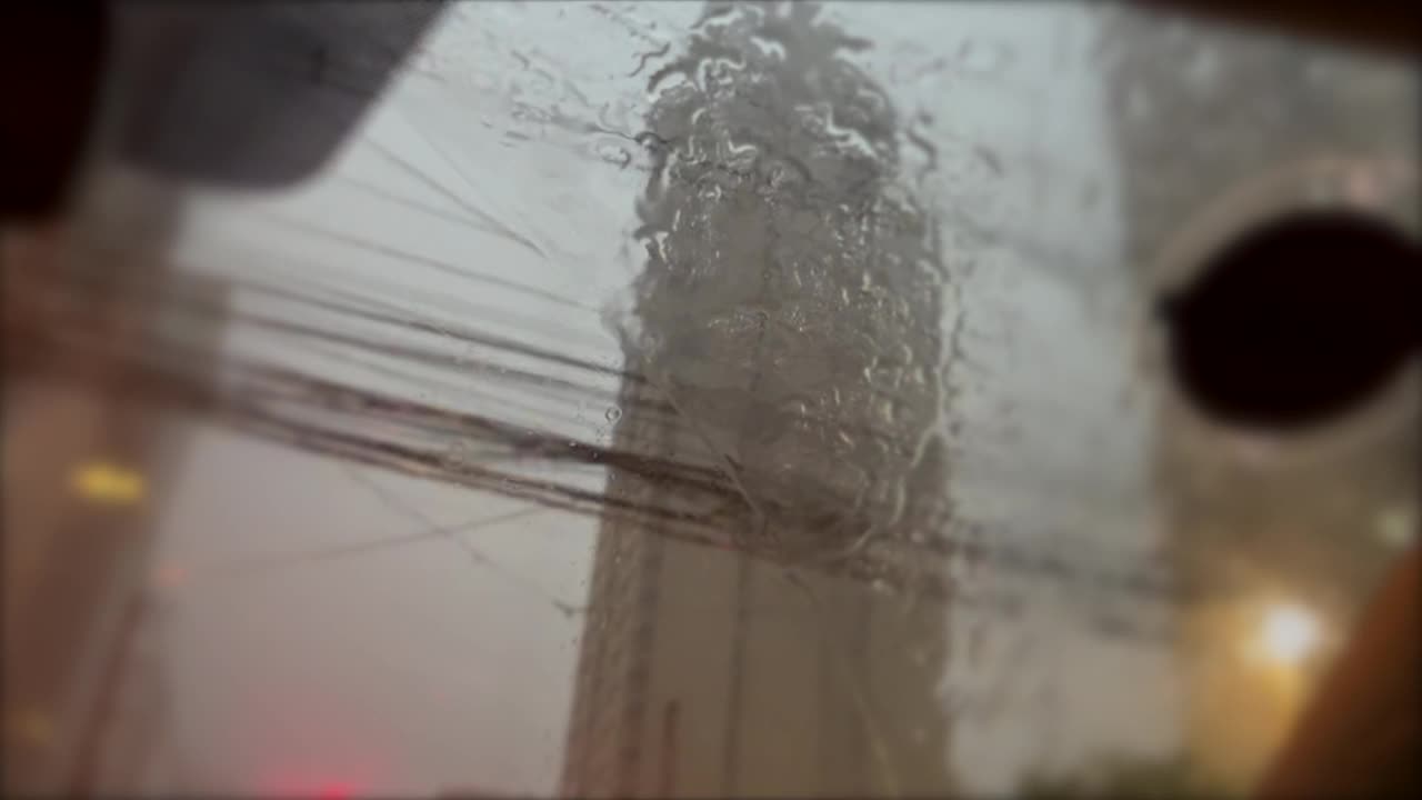 倾盆大雨在汽车挡风玻璃内。雨夜，水滴与城市建筑为背景视频素材