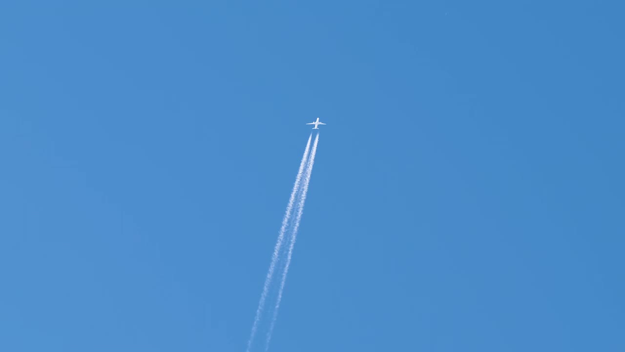 远处的客机在晴朗的蓝天上高空飞行，留下了白色的烟雾痕迹。航空运输概念视频素材