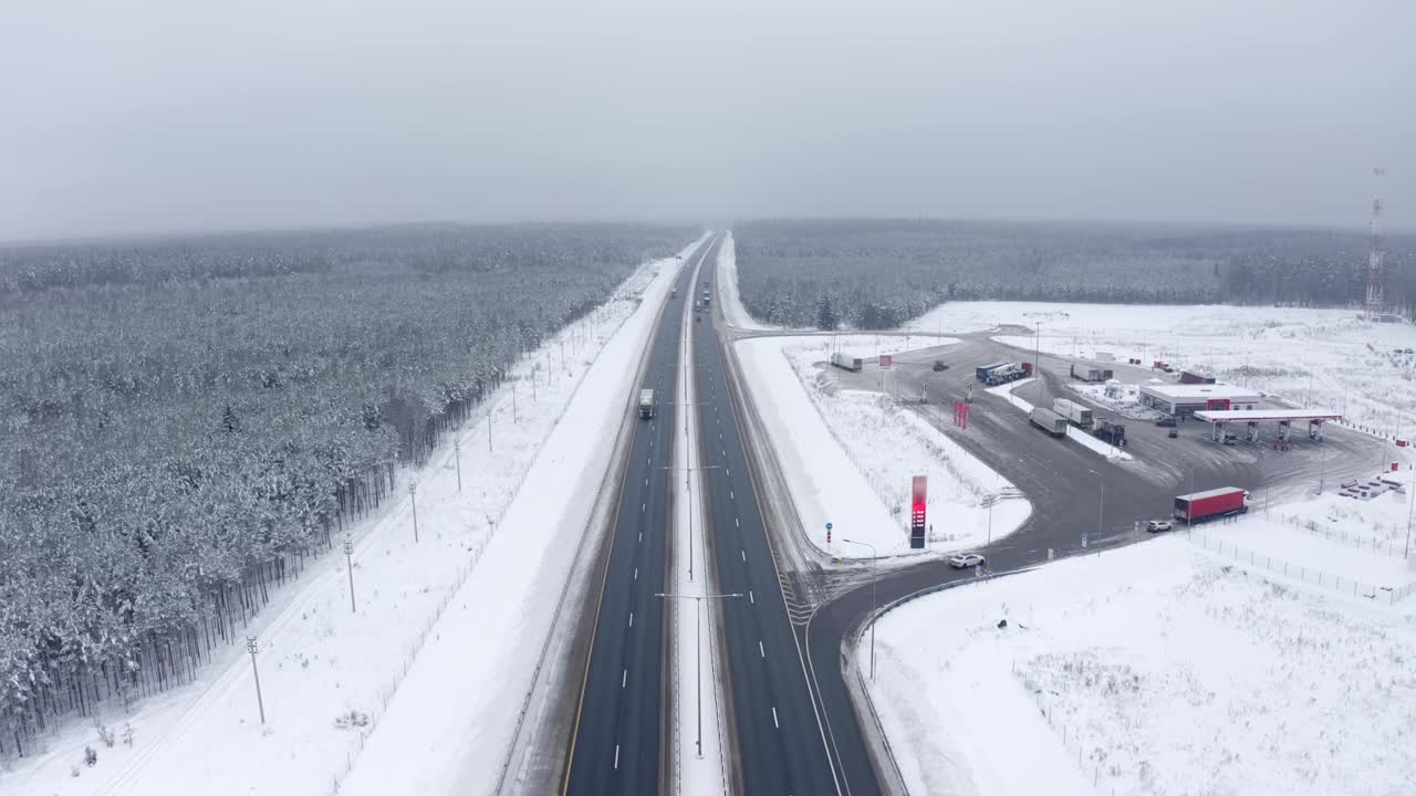 一辆运送货物的卡车在森林中间的道路上行驶，一辆加油站在积雪覆盖的雪地上行驶视频素材