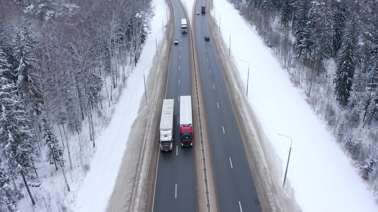 一辆白色轿车和几辆卡车正行驶在白雪覆盖的森林中央的道路上视频素材