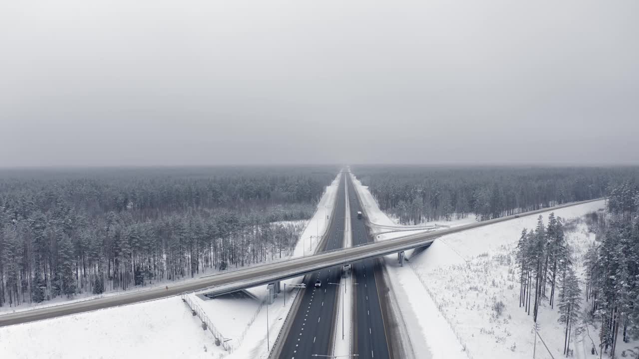 一辆白色的汽车正行驶在白雪覆盖的森林之间的桥下的道路上。视频素材