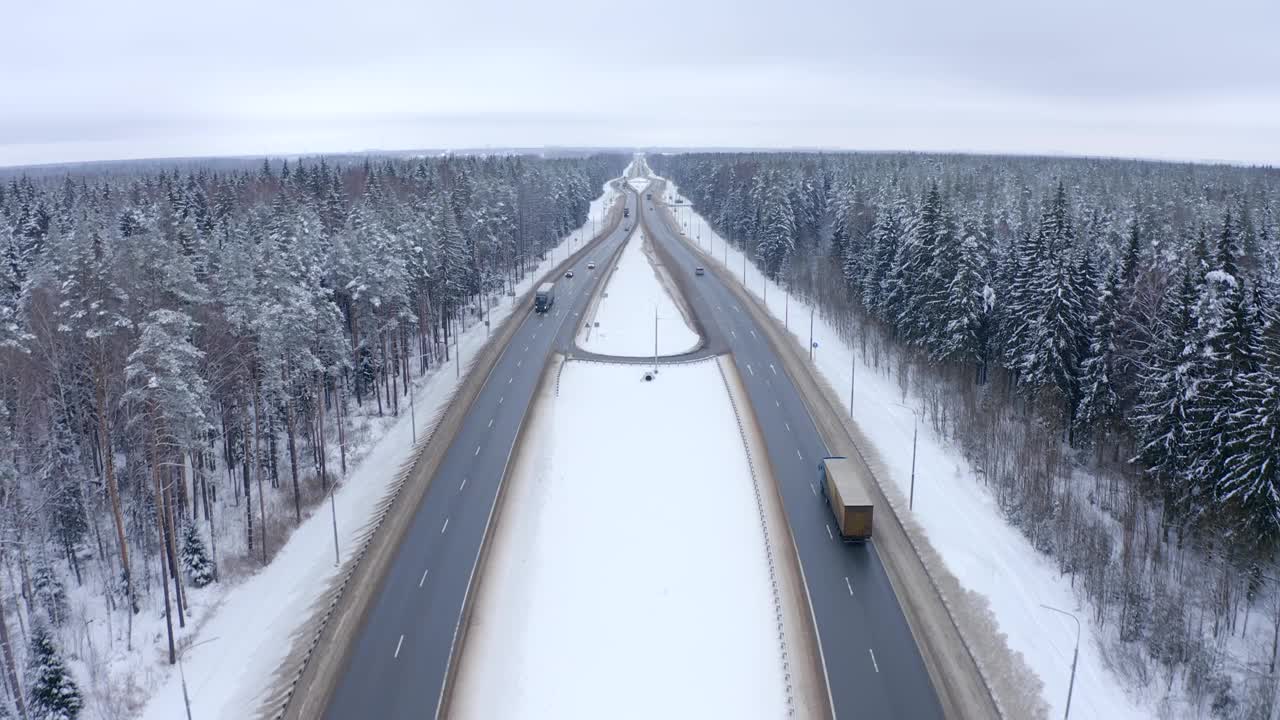 鸟瞰一辆银色汽车和卡车行驶在雪林之间的道路上。视频素材