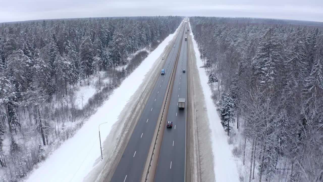 鸟瞰图，几辆汽车和送货车沿着雪林间的道路行驶。视频素材