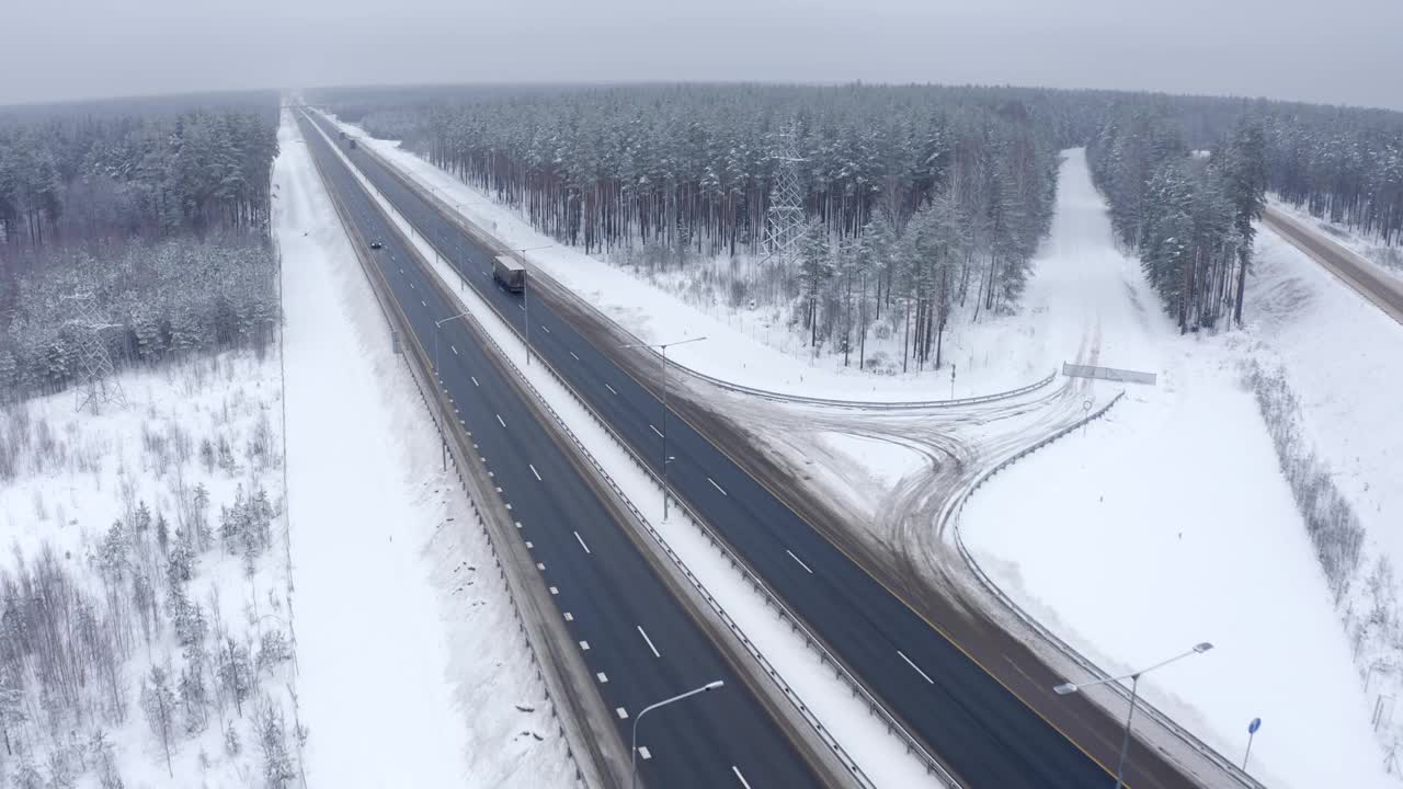 在寒冷的冬天，黑车行驶在白雪覆盖的森林中视频素材