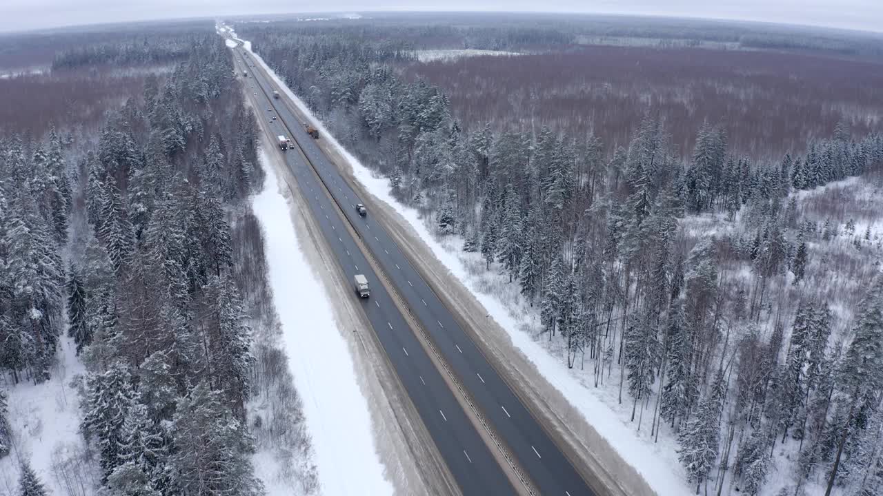 几辆卡车在高速公路上行驶，经过一片白雪覆盖的森林。视频素材