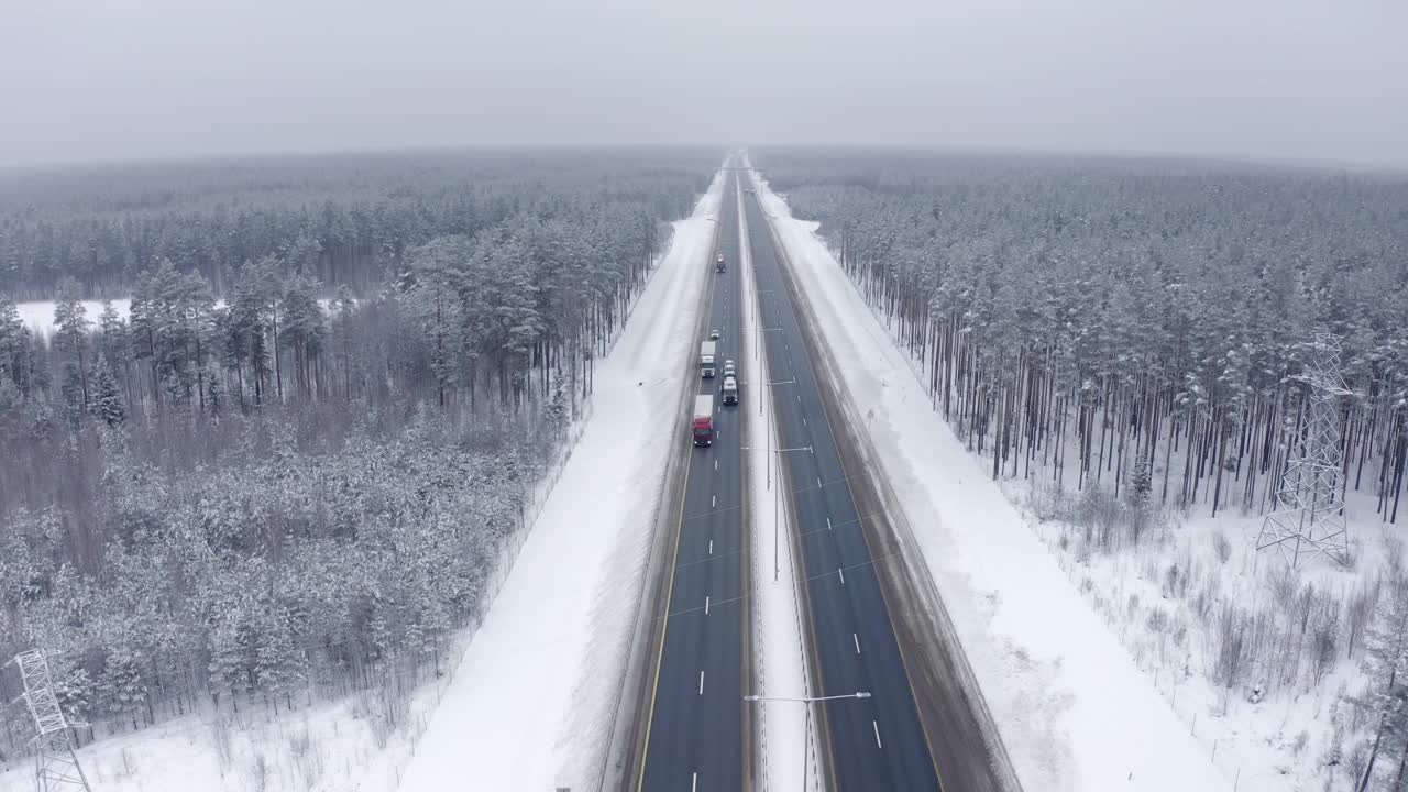 几辆卡车正沿着被雪覆盖的树木之间的道路运输货物视频素材