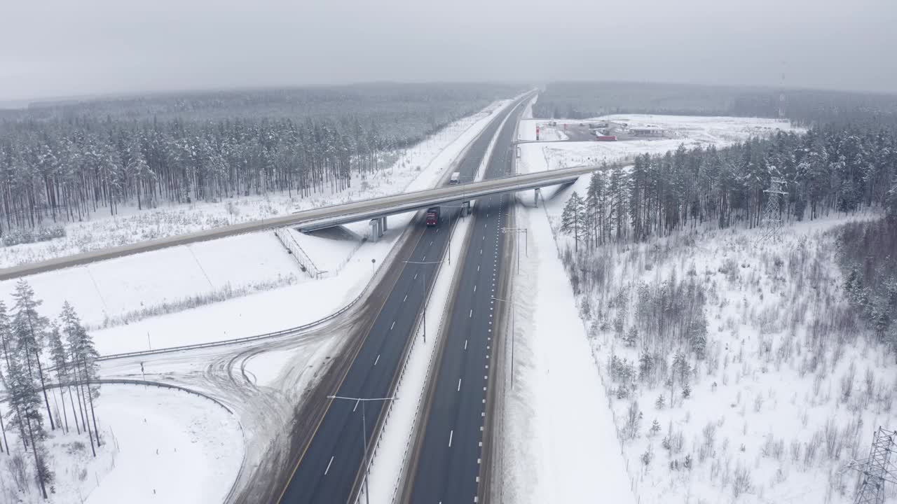 在积雪覆盖的树木中，桥下的道路上，卡车在运输货物视频素材