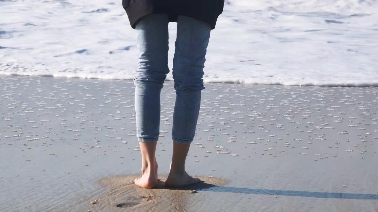 女人或女孩走在大西洋岸边。4K分辨率的近距离观看海浪冲刷裸露的女性腿和海滩。视频素材