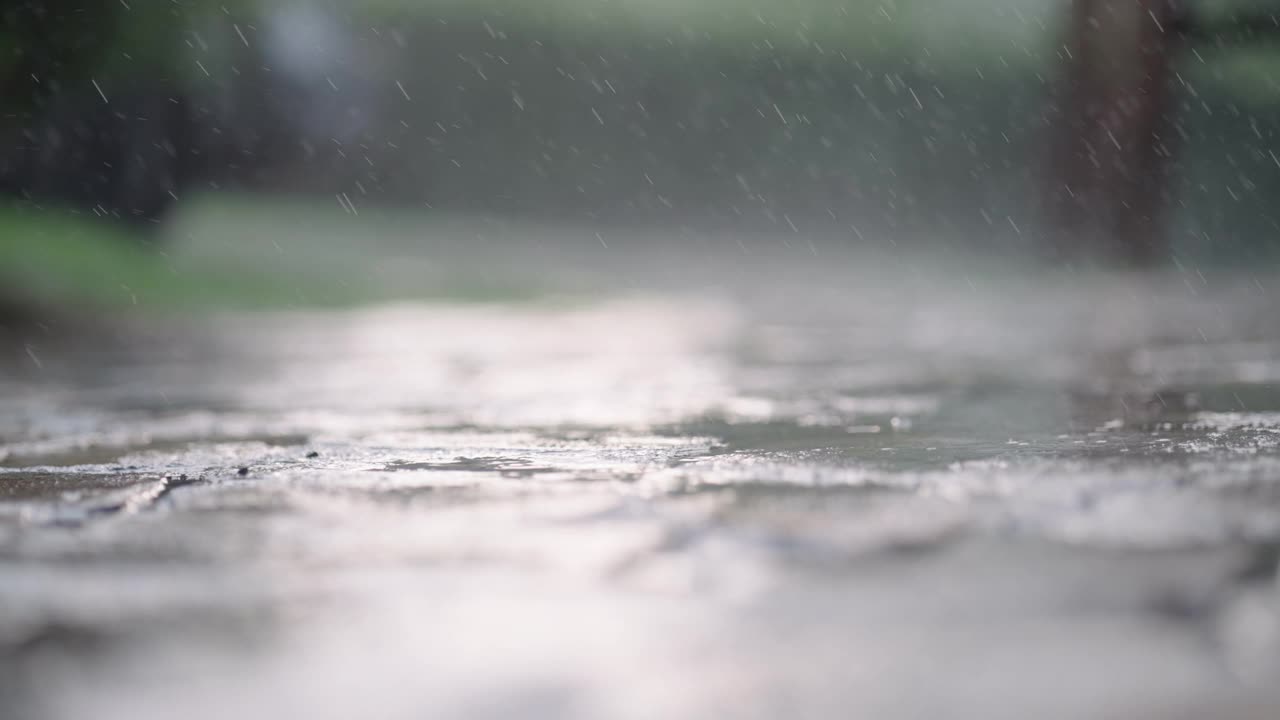 近景:大雨滴溅在潮湿的柏油路上，人行道，慢镜头视频素材