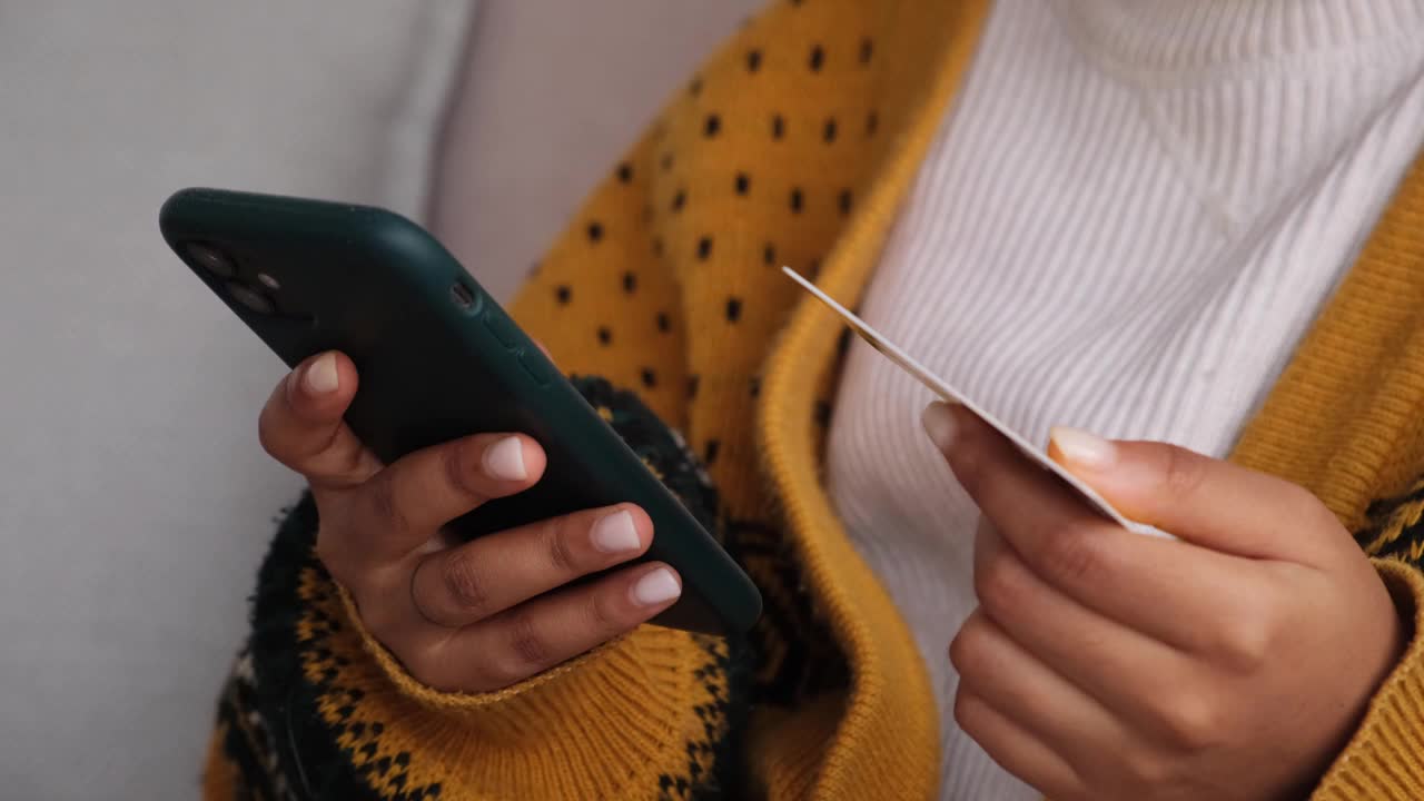 女子手持智能手机网购，用黄金信用卡支付。非裔美国女孩在网上购物时输入信用卡信息。网上购物电子商务送货服务。视频素材