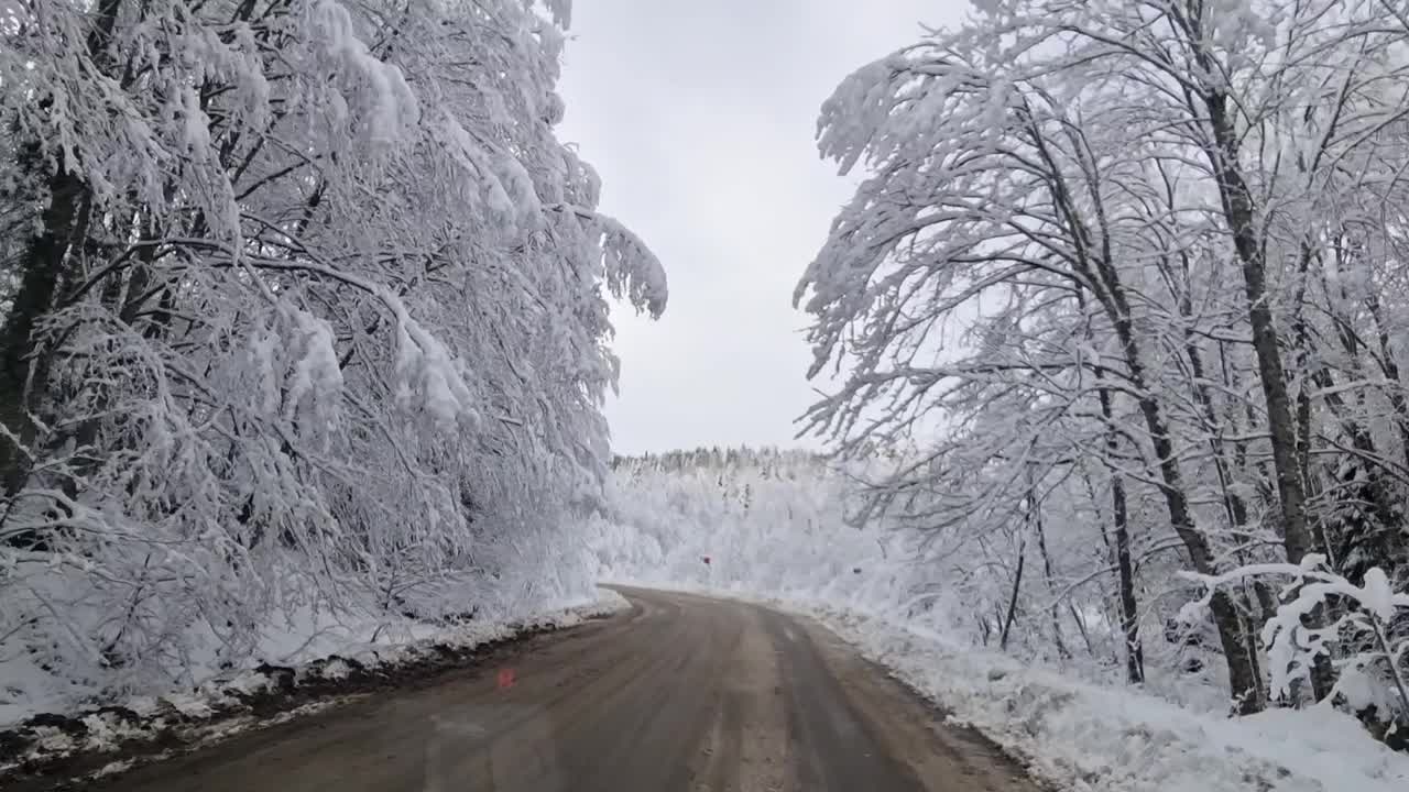 冬天积雪覆盖的道路在山林。射穿挡风玻璃。视频素材