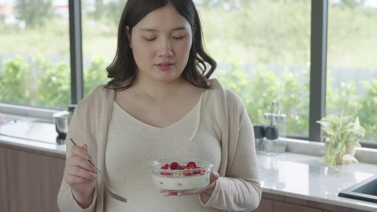 美丽的亚洲孕妇在家里的厨房吃早餐，享受一顿饭。孕妇的美味食物视频素材