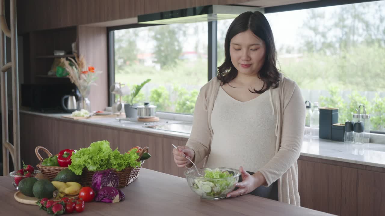 美丽的亚洲孕妇高兴地准备蔬菜沙拉，有机健康食品，在一个舒适的家庭厨房。视频素材